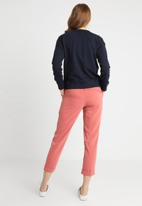 Sudadera de marina con puños acanalados, combinada con pantalones rosa de corte ajustado con dobladillos doblados. Modelo usando zapatillas, de espaldas a la cámara.