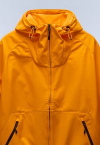 Žlutá bundou na zip s kapucí, vyrobená z hladkého texturovaného materiálu, s nastavitelnými šňůrkami a dvěma bočními kapsami na zip.