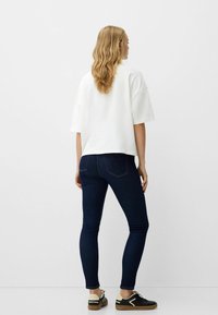 Vit oversized t-shirt med korta ärmar, matchad med mörkblå slim fit-jeans och svarta sneakers med beige detaljer. Enkelt mönster, inga tryck.