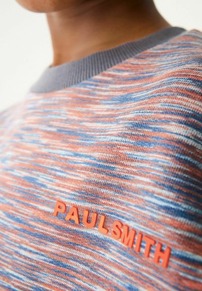 Jersey de punto con un patrón texturizado multicolor en tonos de naranja, azul y gris. Presenta un cuello acanalado gris y un logo naranja.