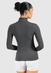 Langärmliges, hochgeschlossenes Oberteil in Dunkelgrau, figurbetontes Design, glatte Textur, kombiniert mit weißen Shorts, die die Rückansicht betonen.