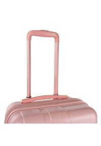 Maleta rígida de color rosa claro con textura estriada, mango retráctil y un acento dorado en el mango superior. Cierre con cremallera visible.
