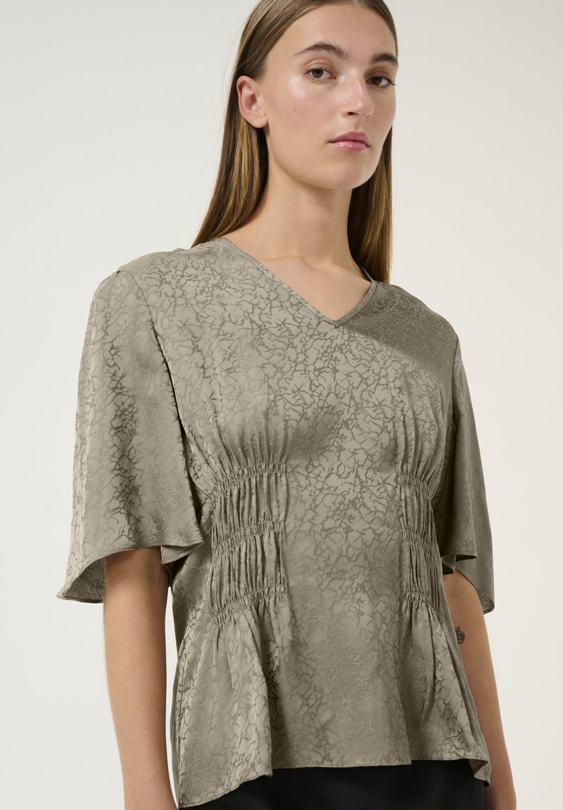 Blusa verde oliva con scollatura a V, dettagli arricciati ai lati e maniche corte e larghe, caratterizzata da un tessuto con una trama testurizzata.