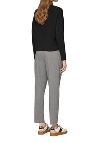 Zwarte pullover met lange mouwen, gecombineerd met lichtgrijze, taps toelopende broek en witte sneakers met zwarte en gouden accenten. Eenvoudige, moderne uitstraling.