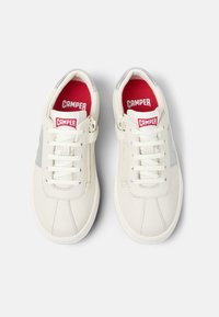 Sneakers in pelle bianca con accenti grigi, dotati di una chiusura con lacci e zip laterale per una facile indossabilità. Soletta rossa con logo "Camper".