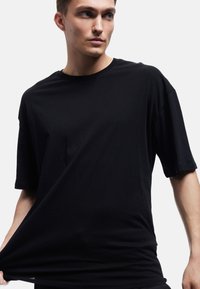 Sort kortærmet t-shirt lavet af blødt, glat stof. Har en rund halsudskæring og en oversized pasform med en let drapering.