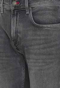 Tmavě šedé džíny z denimu s úzkým střihem, s přední kapsou, měděným knoflíkem a mírným zesvětlením, což vytváří decentní strukturu.