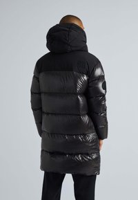 Svart puffjacka med glänsande sektioner, huva och quiltat mönster. Har en logotyp på baksidan och ribbade muddar för värme.