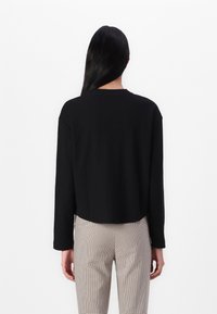 Svart langermet topp med rund hals og kort design, parret med rutete høytlivsbukser. Jevn tekstur, ingen synlige mønstre.