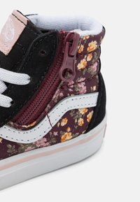 Baskets montantes Vans noires à motif floral avec une fermeture éclair, semelle en caoutchouc blanc et accents roses contrastants.
