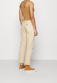 Jeans beige de cintura alta con un ajuste relajado, que presentan bolsillos traseros y costuras decorativas, combinados con zapatillas altas de lona marrón.