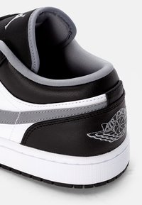 Gros plan sur le talon d'une basket noire, blanche et grise avec un col rembourré et le logo ailé Air Jordan brodé en gris.
