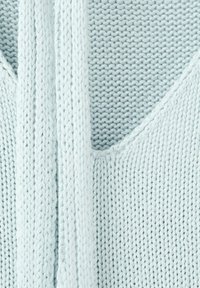 Jasnoniebieska dzianina z bliska z grubymi splecionymi sznurami leżącymi na niej, ukazującymi szczegółowe wzory ściegów i miękką fakturę.