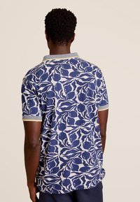 Poloshirt met korte mouwen met een blauw-wit abstract bladpatroon, lichte grijze kraag en gele accenten op de mouwen.