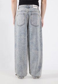 Vaqueros de mezclilla de pierna ancha de color azul claro con cintura alta, con bolsillos traseros, costuras tonales y etiqueta en la cintura. Diseño transpirable y casual.