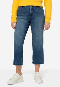 Jeans de mezclilla cortos en azul oscuro con rayas verticales, con una cintura alta y un dobladillo deshilachado. Combinados con zapatillas blancas.