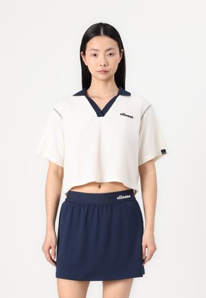 Polo corto de manga corta color crema con cuello navy, que presenta un logo y un ribete a rayas. Combinado con una falda con cintura elástica navy. Textura suave.