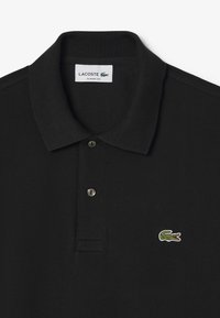 Camisa polo negra con cuello tipo blazer, dos botones y logotipo de cocodrilo bordado en verde. Fabricada en tejido de algodón texturizado. Corte clásico.