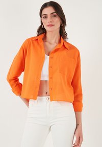 Orange linen shirt with a button-up front, collar, and a chest pocket. Pairing with white high-waisted jeans for contrast.