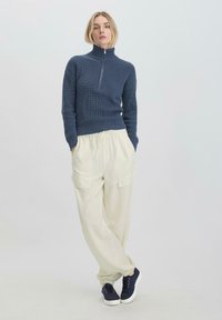 Navy geribbelde trui met hoge kraag en halve rits, gecombineerd met ontspannen crèmekleurige cargobroek met zijzakken en elastische boorden.