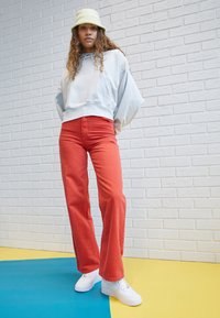 Light blue oversized hoodie, red wide-leg jeans, white sneakers, and a light green bucket hat, set against a colorful background.