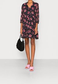 Floral black dress with 3/4 sleeves, tiered design, paired with a textured black bag and pink cross-over sandals.