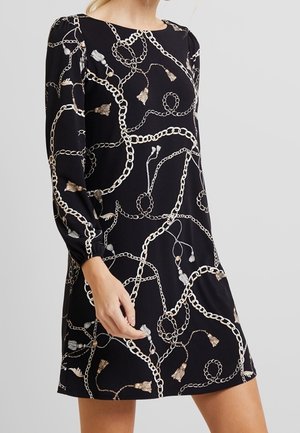 Musta pitkähihaiset mekko, jossa beige-valkoinen ketju- ja tupsukuosi, pyöreä pääntie ja rento, polveen ulottuva istuvuus.