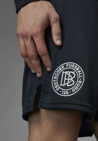 Black sports shorts with a ribbed texture feature a circular white logo reading "DEUTSCHER FUSSBALL-BUND" and "125." Hem has a small cutout.