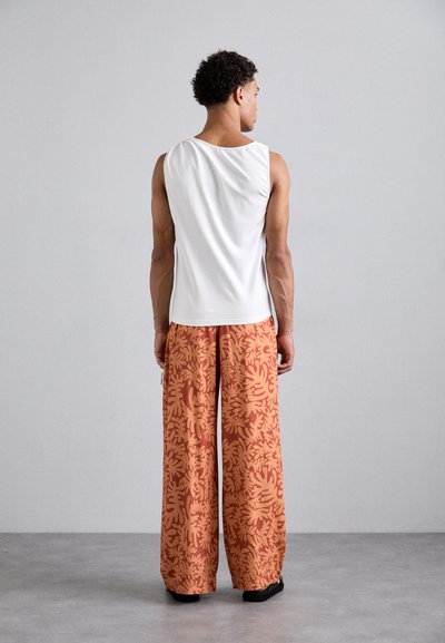 White sleeveless top with an open back, paired with wide-leg orange pants featuring a coral pattern, set against a neutral background.