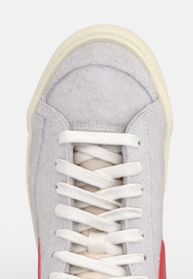 Sneaker in suede grigio chiaro con finitura texture, lacci bianchi e un accento rosso ai lati. Presenta una suola in gomma color crema.
