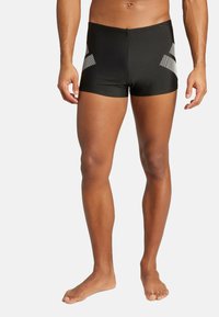 Crne kupaće hlače sa prilagođenim dizajnom, sivi dijagonalni akcenti. Izrađene od glatkog materijala, krojene iznad koljena, pogodne za vodene aktivnosti.