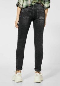 Svarta smala jeans med en urtvättad yta, med två bakfickor och uppvikta benslut, i kombination med vita sneakers.