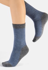 Calcetines con patrón de espiga en azul y gris, fabricados en material suave, con un puño de canalé gris oscuro y refuerzo en el talón y la punta.