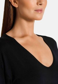 Zwarte top met een diepe V-hals, gemaakt van gladde stof, met korte mouwen en een losse pasvorm. Minimalistisch ontwerp zonder extra accenten.