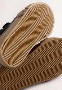 Melnu sporta apavu zolēm ar zivju kaula rakstu; gumijas materiāls; bēša krāsas akcenti; fakturētas virsmas; uz papēža redzama logotipa iespiešana.