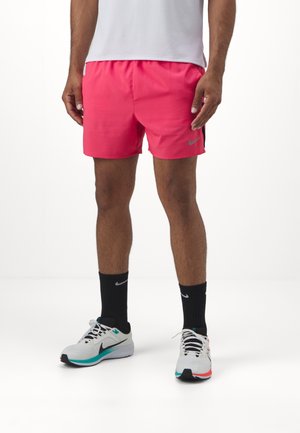 Men's pink athletic shorts with an elastic waistband; paired with black crew socks and white athletic shoes featuring turquoise and red accents.