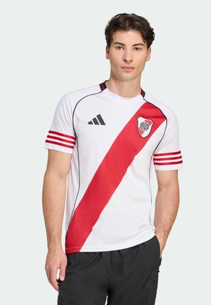 Weißes Fußballtrikot mit einem roten diagonalen Streifen, schwarzen Akzenten, einem runden Kragen und rot gestreiften Ärmeln. Enthält ein Logo auf der Brust.