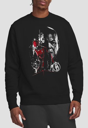 Schwarzer Sweatshirt mit einem grafischen Design in Rot- und Weißtönen, das eine Figur vor einer Stadtlandschaft zeigt.