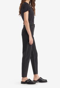 Jeans negros de cintura alta con un corte recto, combinados con una blusa negra de manga corta y zapatos negros sin cordones con un detalle de hebilla.