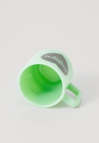 Taza de plástico verde claro, con forma redondeada, inclinada de lado, presenta un logo de color gris oscuro en un lado, textura suave y un asa robusta.