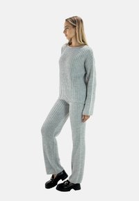 Grauer, gerippter Strickpullover und Hosen-Set mit lässiger Passform, das lange Ärmel und eine weite Beinform aufweist, kombiniert mit klobigen schwarzen Schuhen.