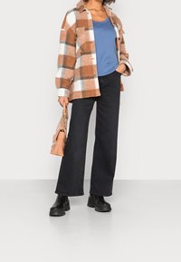 Koszula z wełny w kratkę w brązowym, białym i szarym kolorze; niebieski top na ramiączkach; czarne szerokie dżinsy; czarne botki za kostkę; mała tanie torebka z łańcuszkiem.