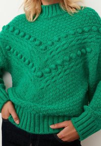 Groene gebreide trui met een hoge kraag, voorzien van textuurpatronen, geribbelde manchetten en een gezellige, chunky ontwerp met dimensionale bobbels.
