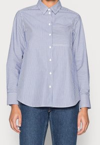 Modrá a bílá pruhovaná košile na knoflíky s límečkem, dlouhými rukávy a kapsou na levé straně hrudi; vyrobená z hladké látky s přizpůsobeným střihem.