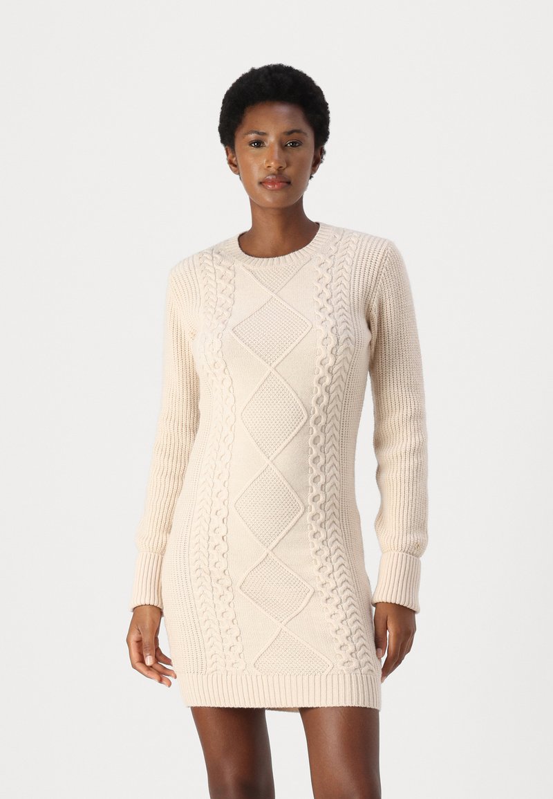 Strikket kjole i beige med teksturerte kabelmønstre, lange ermer, rund hals og ribbestrikkede mansjetter og nederkant. Fitted silhuett.