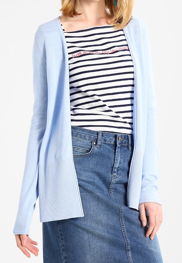 Lichtblauwe cardigan met geribde accenten, gedragen over een marineblauwe en witte gestreepte shirt met tekst. Gepaard met een denimrok.