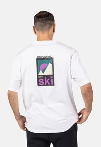 Bílá bavlněná tričko s barevným grafickým potiskem na zadní straně, který zobrazuje hory, purpurové slunce a výrazný text "ski" v růžové barvě.