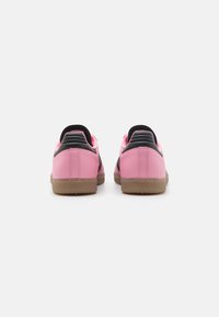 Pink sneakers with black accents, low-top design, smooth synthetic material, featuring a textured heel and rubber outsole.