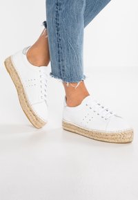 Vita lädersneakers med vävda jute-sulor, som har sex snörhål, perforerade detaljer och något upphöjda tår; bärs med fransiga blå jeans.