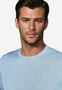 Hellblauer, strukturierter Strickpullover mit Rundhalsausschnitt und weicher Oberfläche; enganliegend; keine sichtbaren Muster; minimalistische Gestaltung.